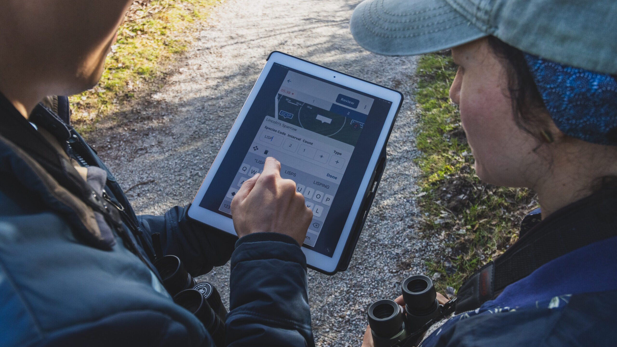 Two birdwatchers are looking at a tablet that is display the NatureCounts point count tool.